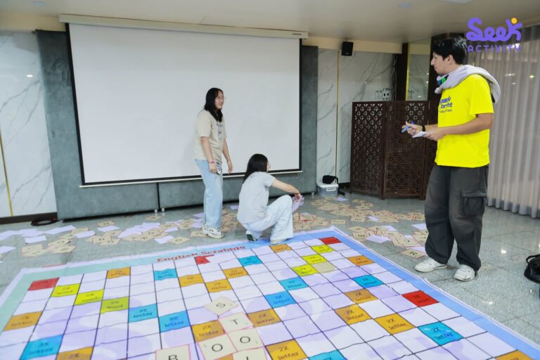 นักเรียนร่วมสนุกกับเกมต่อคำศัพท์ภาษาอังกฤษ Giant Scrabble ขนาดใหญ่บนพื้น โดยมีวิทยากรคอยให้คำแนะนำ