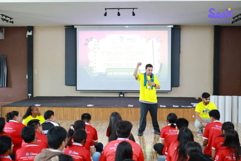 วิทยากรถือไมโครโฟนนำกิจกรรมด้านหน้าห้อง ขณะที่นักเรียนโรงเรียนพระนารายณ์นั่งร่วมกิจกรรม