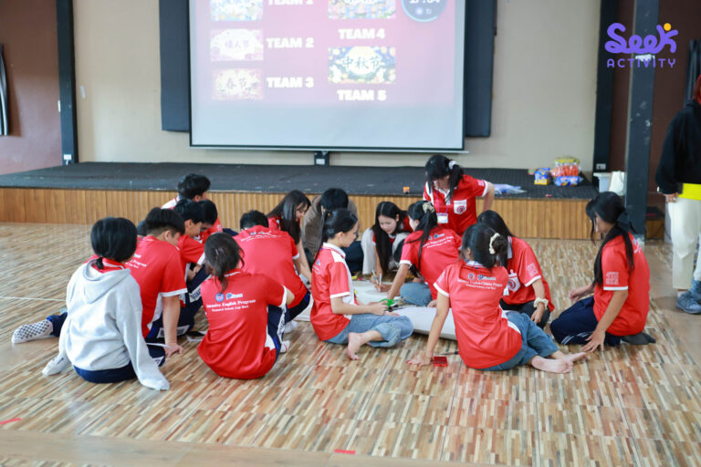 นักเรียนนั่งทำงานกลุ่มบนกระดาษ โดยมีภาพและข้อความเกี่ยวกับเทศกาลจีนแสดงบนจอ